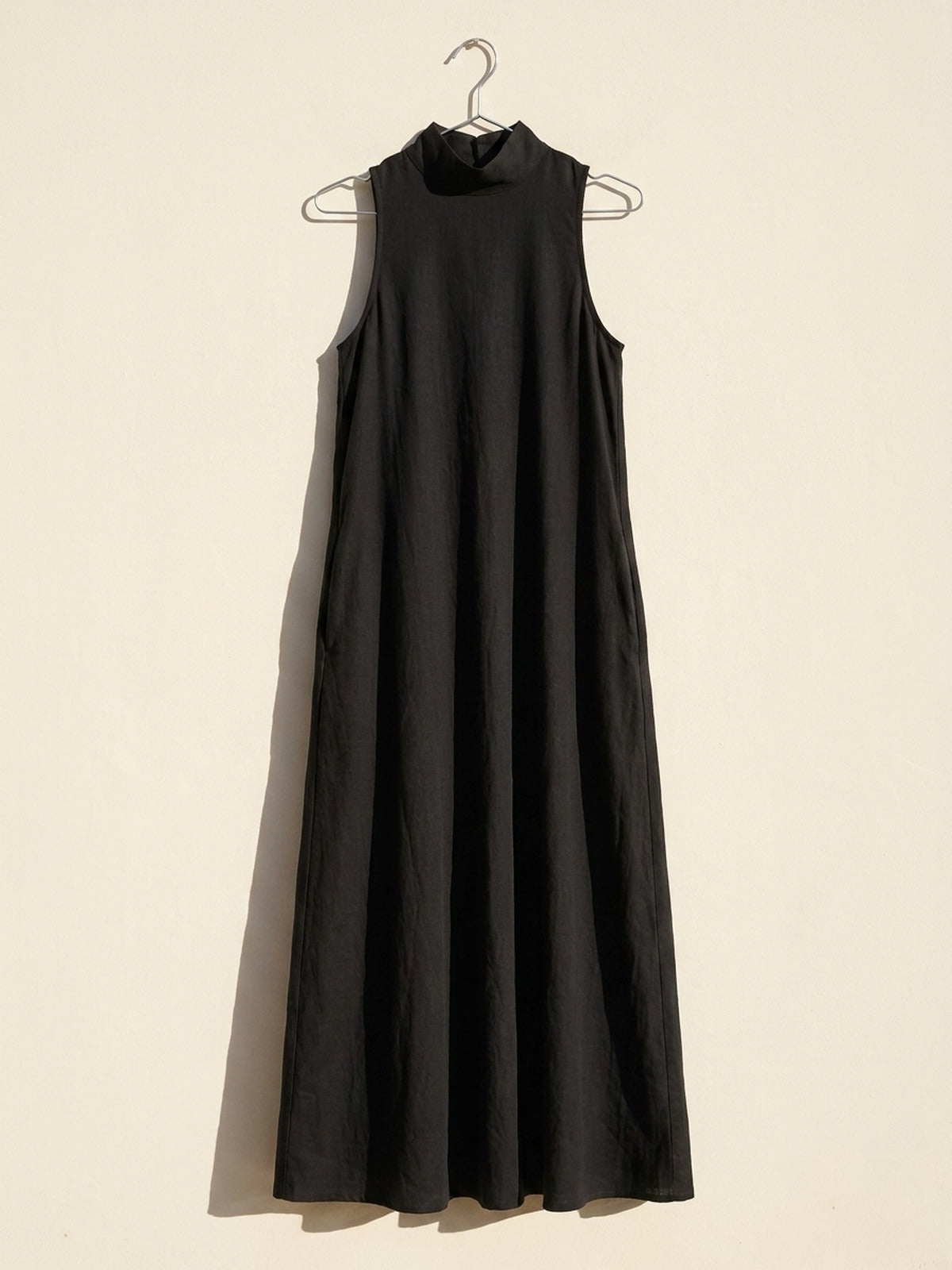 Vestido negro Caterina colgado de una percha sobre pared crema, para ver su forma real
