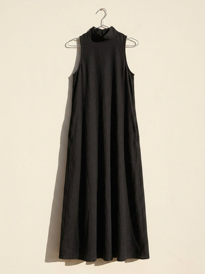 Vestido negro Caterina colgado de una percha sobre pared crema, para ver su forma real