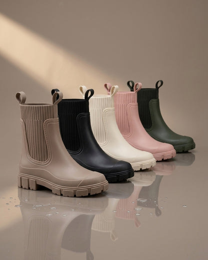 Los cinco colores de la bota de agua Nerea: topo, negro, crudo, rosa y verde militar, sobre suelo mojado