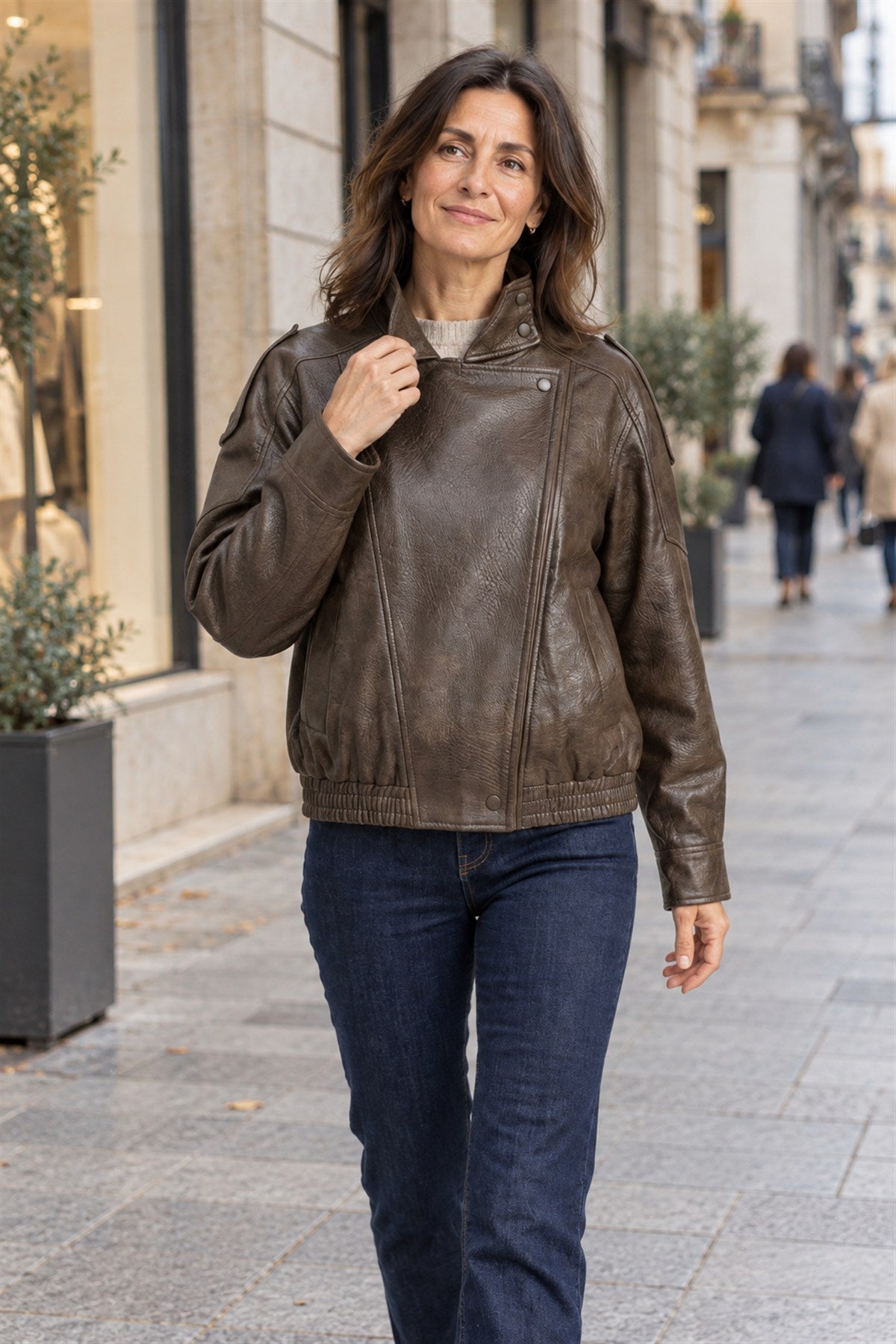 Clara en marrón con vaqueros, andando por una calle de escaparates en otoño